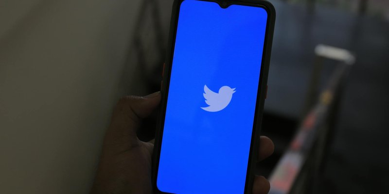 Close-up of a hand holding a smartphone displaying the Twitter app screen.