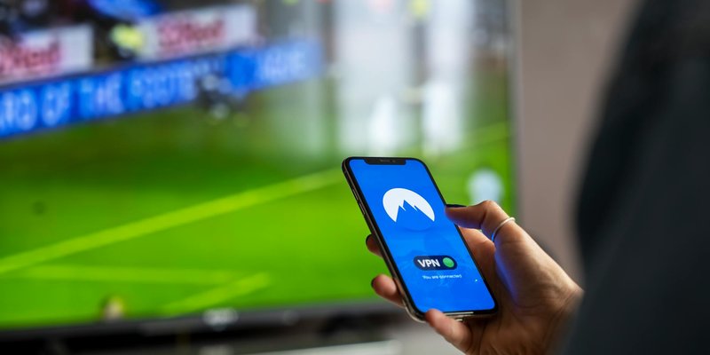 Close-up of a person holding a smartphone with a VPN app, streaming sports on TV.