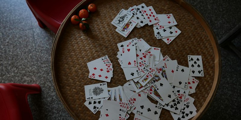 Aerial shot of scattered playing cards on a wicker table with red chairs and small tomatoes.
